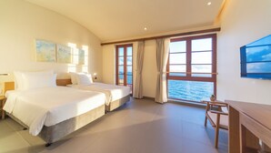 Habitación de hotel con dos camas, un escritorio y un ventanal con vista al mar.