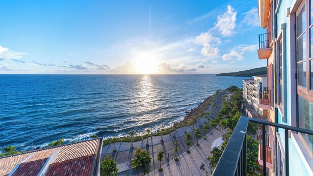 Vista al mar desde un balcón con cielo despejado y el sol poniéndose o saliendo sobre el agua.