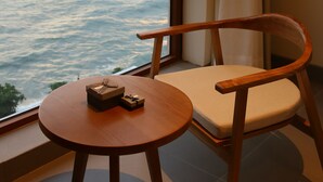 Una habitación con una silla de madera y una mesita junto a una ventana con vistas al agua.