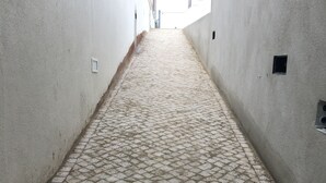 A narrow alleyway with cobblestone pavement, flanked by plain white walls.