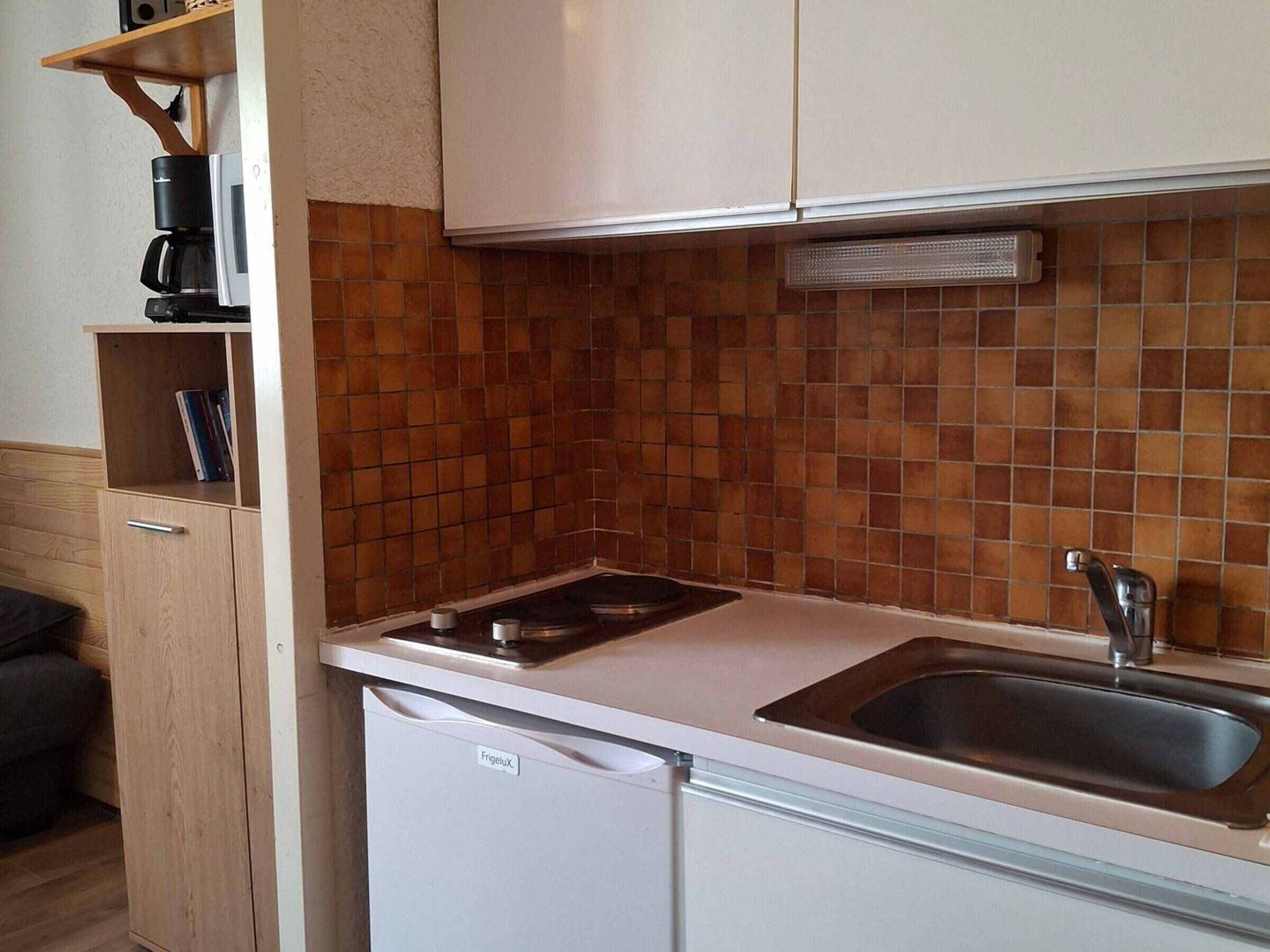 Cocina compacta con encimera blanca, estufa integrada, un lavabo y un refrigerador Frigelux.