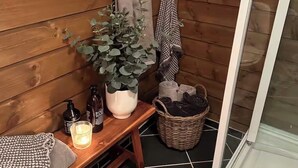 Una cabaña de madera con un banco, una planta en maceta, una vela y una cesta de objetos.