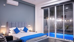 Et moderne soveværelse med en stor seng, en glasdør der fører til et poolområde, og en vægmonteret aircondition.
