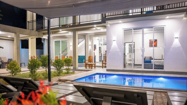 Et udendørs poolområde med liggestole, et overdækket siddeområde og en trappe, der fører til en etage over.
