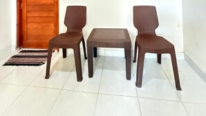 Une pièce avec une porte en bois, deux chaises marron, une petite table et un tapis à motifs.
