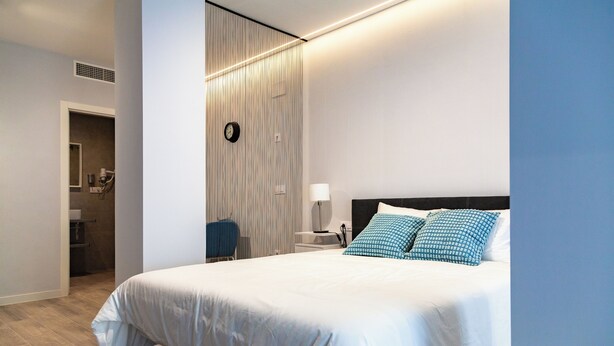 Ein modernes Hotelzimmer mit einem großen Bett, einem Nachttisch mit Lampe und Blick ins Badezimmer.