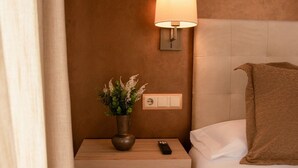 A hotel room with a bed, a nightstand with a lamp, a remote control, and a potted plant. - HOSTAL AGORA (Novetlè)