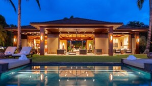A luxurious resort with a large pool, outdoor seating, and a well-lit patio area. - Laueki 5 – Ocean View Estate | Onsite Staff & Daily Housekeeping (Kailua Kona)