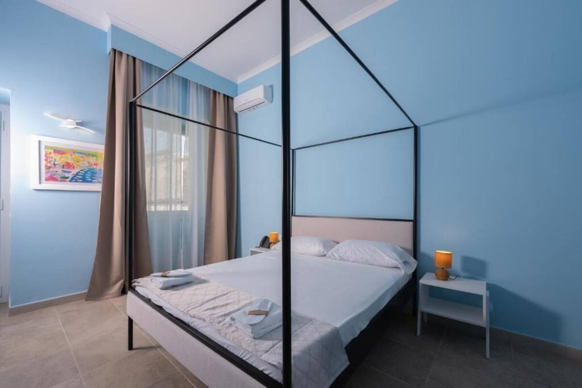A bedroom with a four-poster bed, a bedside table with a lamp, and a wall-mounted air conditioner.
