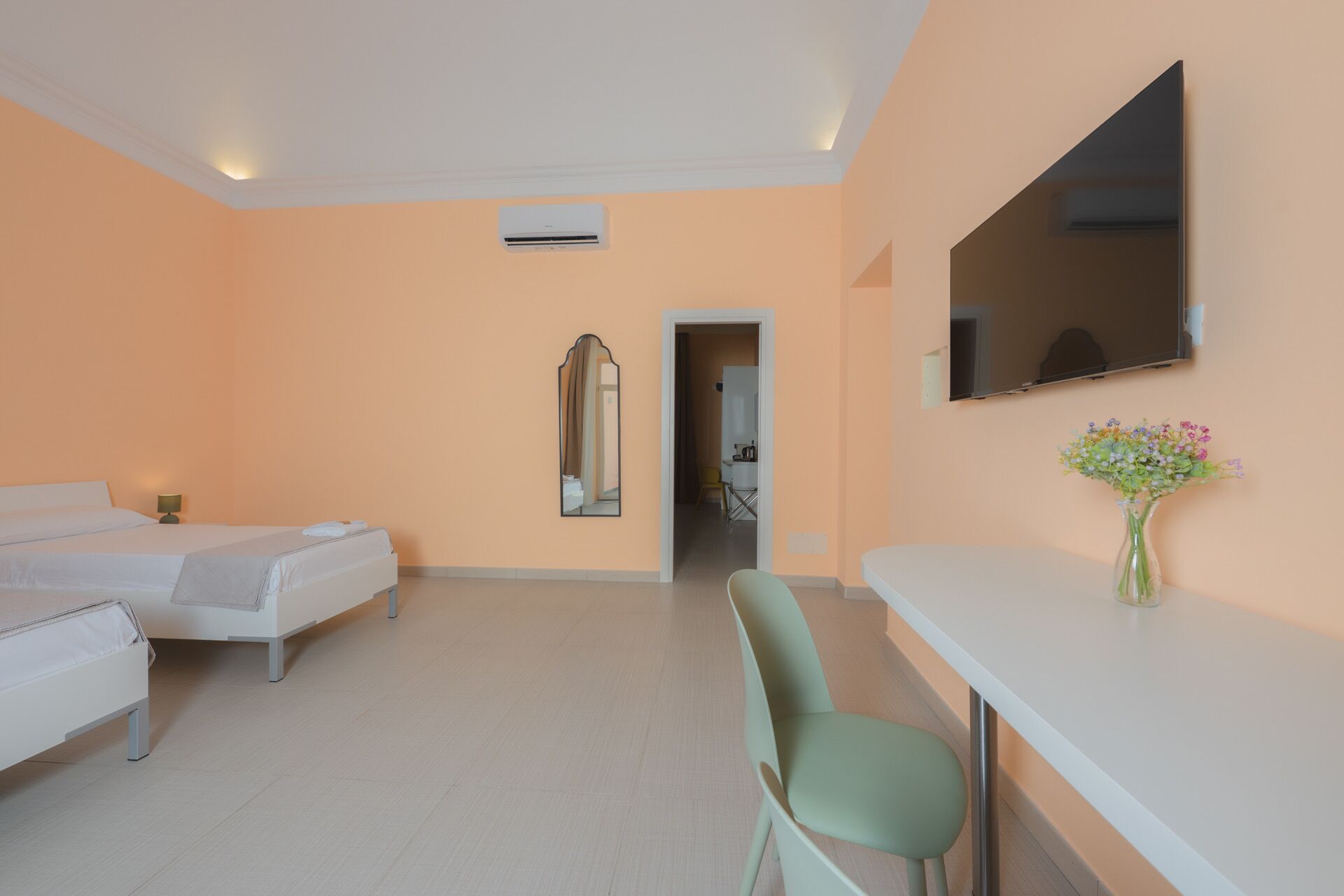 A hotel room with two beds, a desk, a chair, a mirror, and a TV.