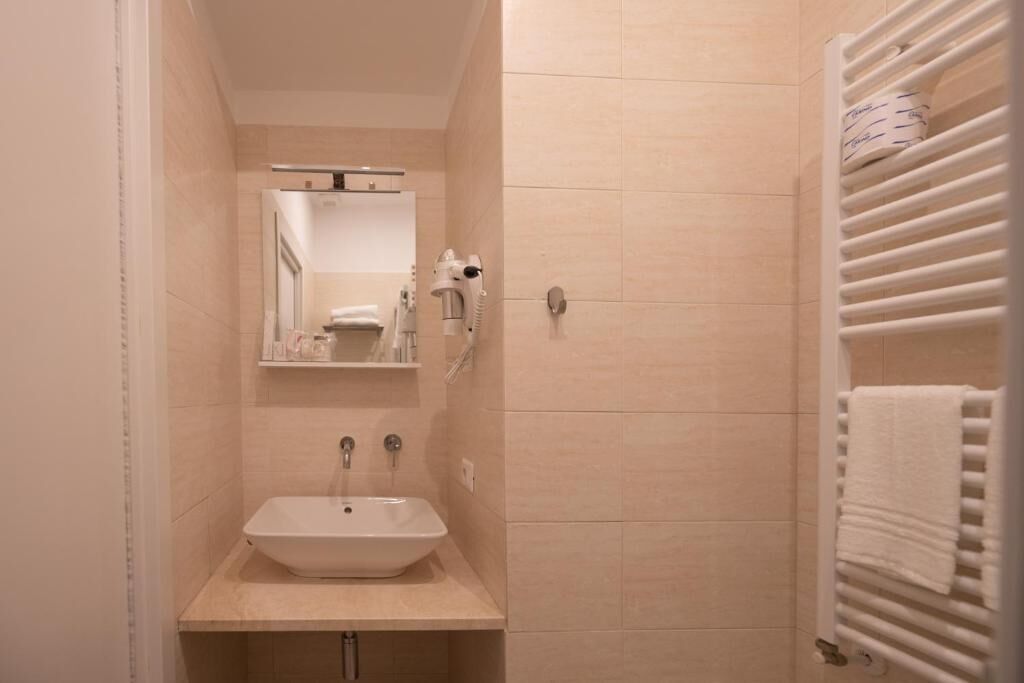 A narrow bathroom with a pedestal sink, a mirror, and a towel rack.