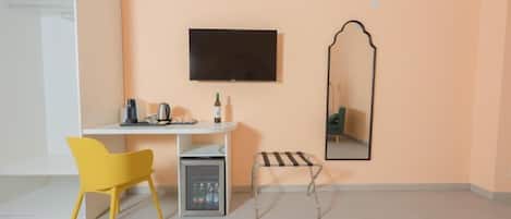 A small, modern room with a white desk, a yellow chair, a mini-fridge, a television, and a mirror.