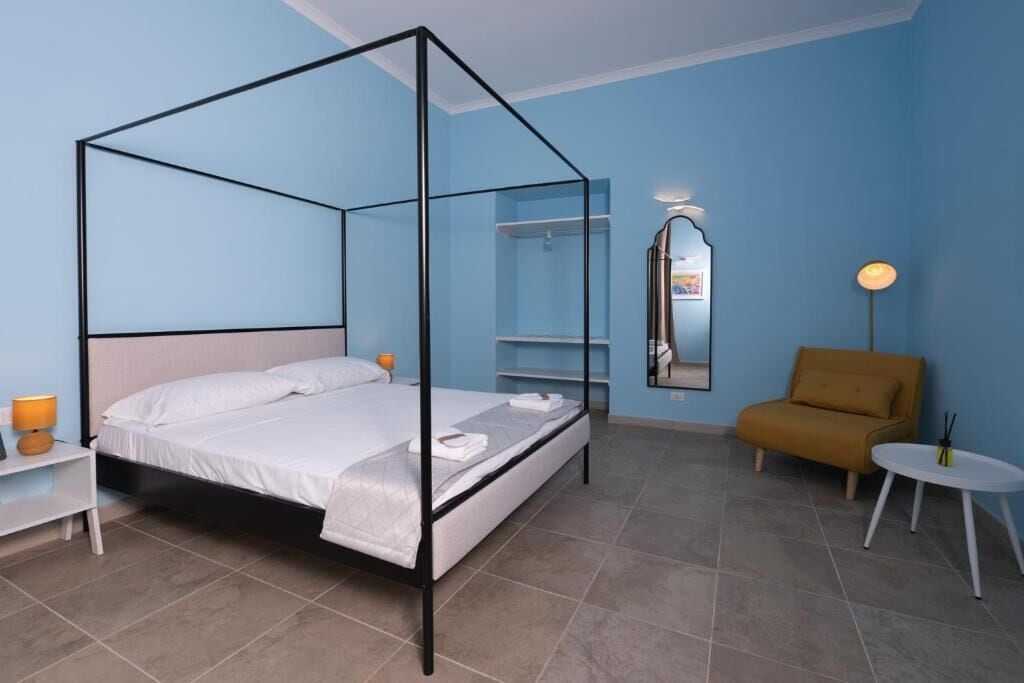 Une chambre à coucher avec un lit à baldaquin, une table de chevet, une chaise, une petite table et un miroir au mur.