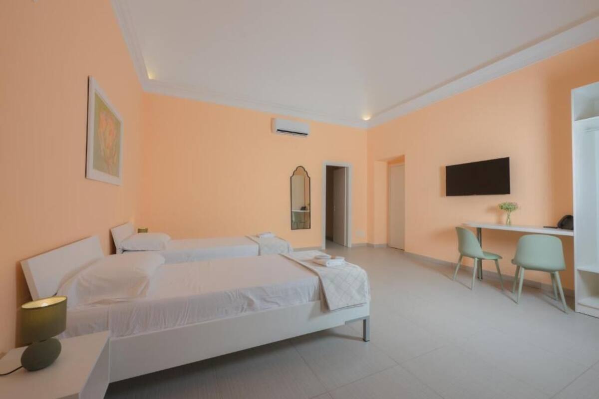 A hotel room with two beds, a desk with a chair, a TV, and a painting on the wall.