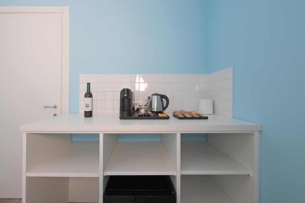 Een compacte kitchenette met een wit aanrecht, een wijnfles, een koffiezetapparaat en een waterkoker.