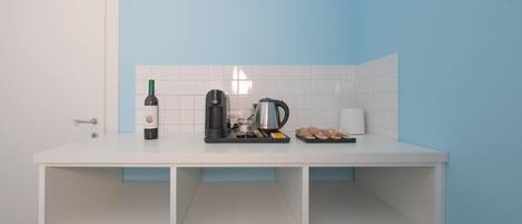 Een compacte kitchenette met een wit aanrecht, een wijnfles, een koffiezetapparaat en een waterkoker.