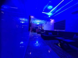 Un pasillo con techo iluminado en azul y una zona de bar al fondo.