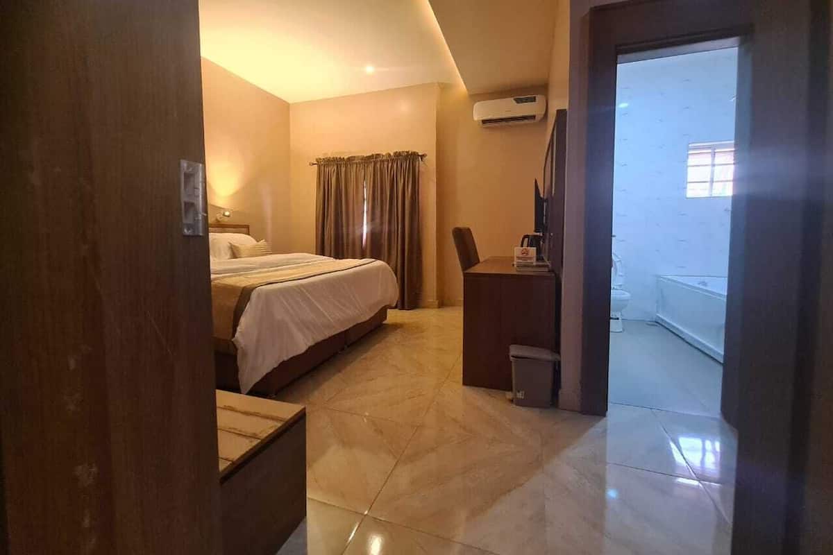 Une chambre d’hôtel avec un lit, un bureau et une salle de bain, visibles à travers une porte ouverte.