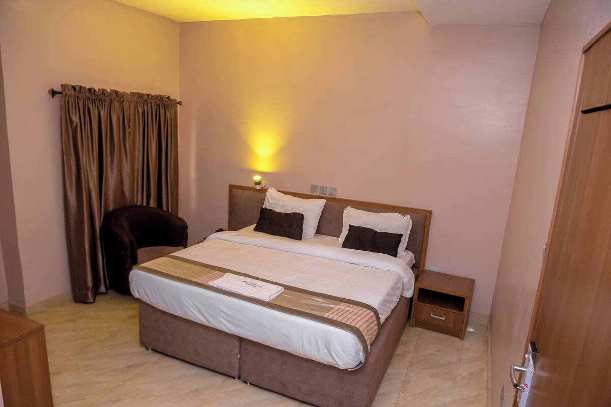 Une chambre d’hôtel avec un grand lit, une table de chevet, une chaise et une lampe fixée au mur.