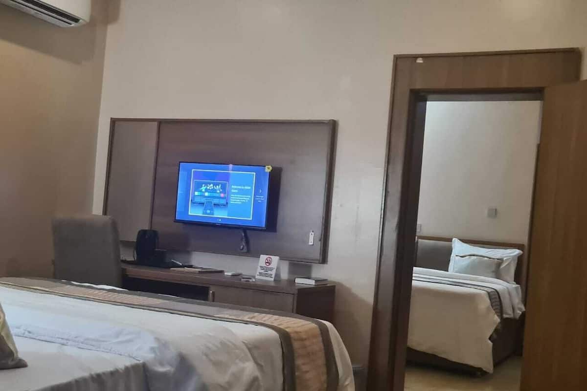Une chambre d’hôtel comprenant un lit, un bureau avec un ordinateur, une télévision et une porte donnant sur une autre pièce.