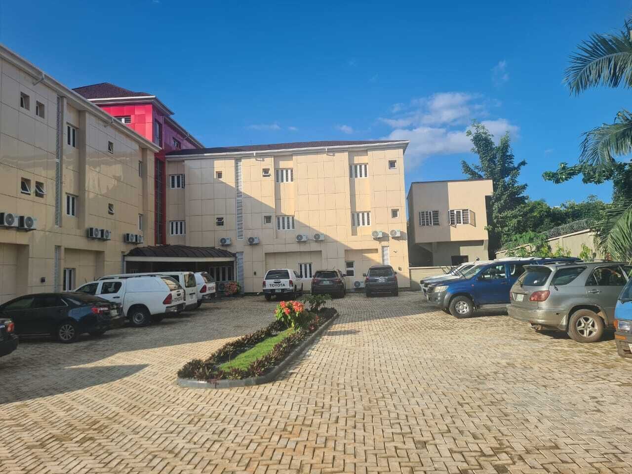 Un'area di parcheggio con diverse auto, un vialetto lastricato e un edificio con numerose finestre e condizionatori.