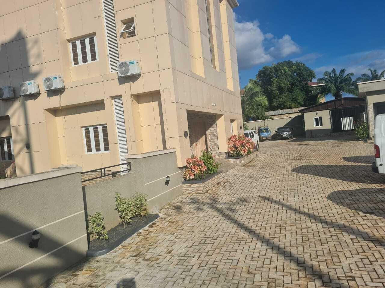Ein mehrgeschossiges Gebäude mit Klimaanlagen, einer gepflasterten Auffahrt und einer kleinen Gartenanlage mit Pflanzen.