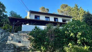 A two-story house with a tiled roof, a balcony, and a stone staircase leading to the entrance.