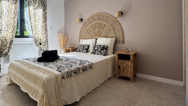 A bedroom with a bed, bedside tables, a headboard, and a window with curtains.