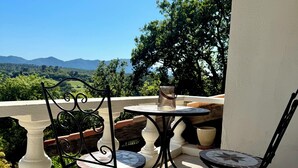 A balcony with a table and chairs, offering a view of a mountainous landscape.