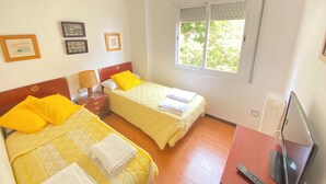 A hotel room with two beds, a TV, and a window with blinds. - Beach apartment, in front of the sea! (Caldes d'Estrac)