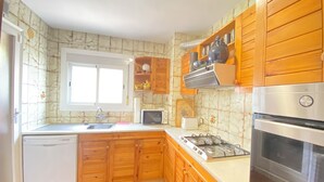 A compact kitchen with wooden cabinets, a built-in oven, a gas stove, a dishwasher, and a window. - Beach apartment, in front of the sea! (Caldes d'Estrac)