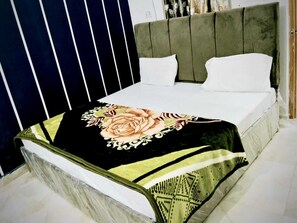 Een bed met een bloemenbedekking, een bekleed hoofdeinde in het groen en witte kussens.