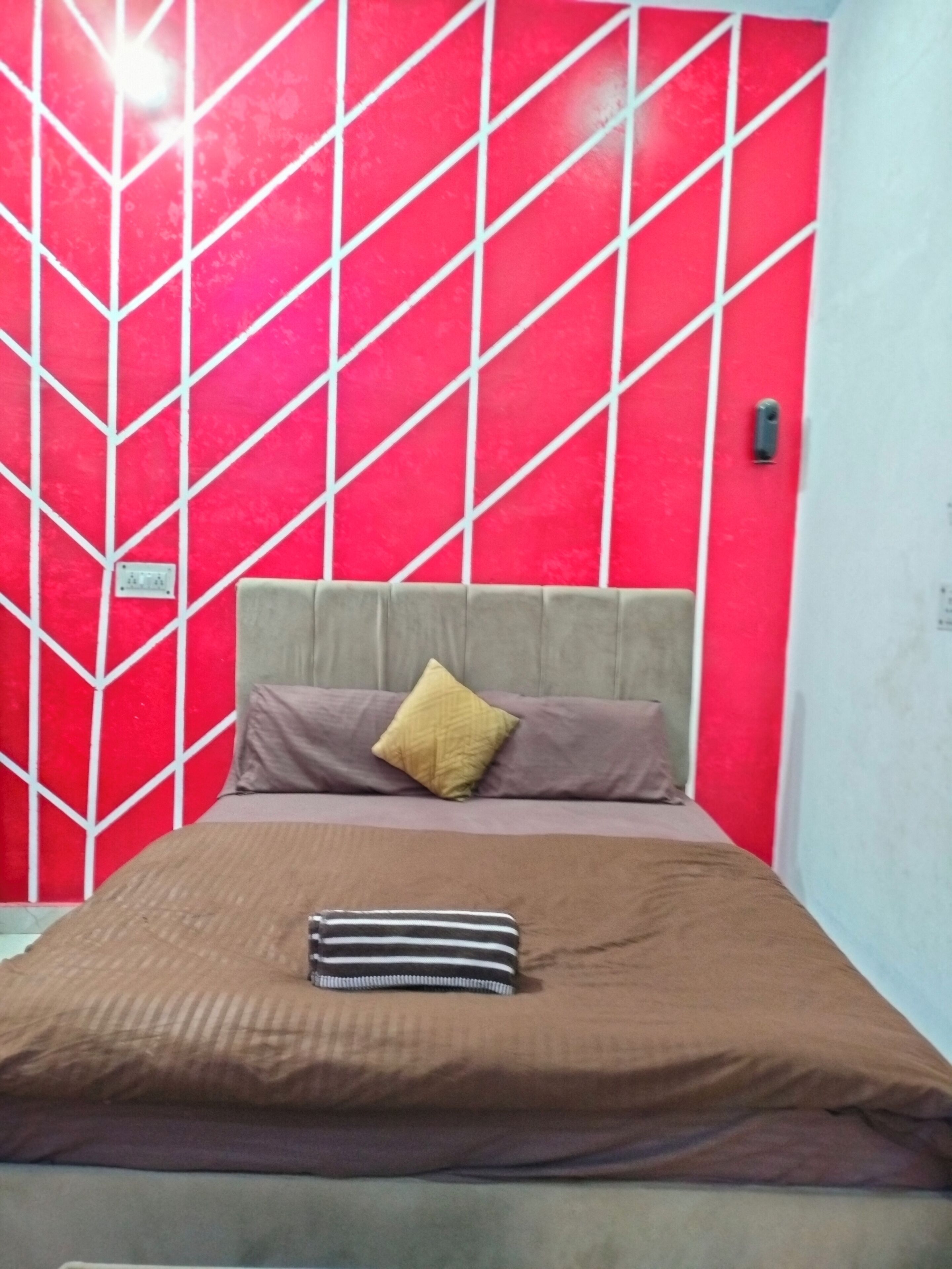 A bed with a striped pillow and a brown bedspread in a room with a red and white geometric wall pattern.