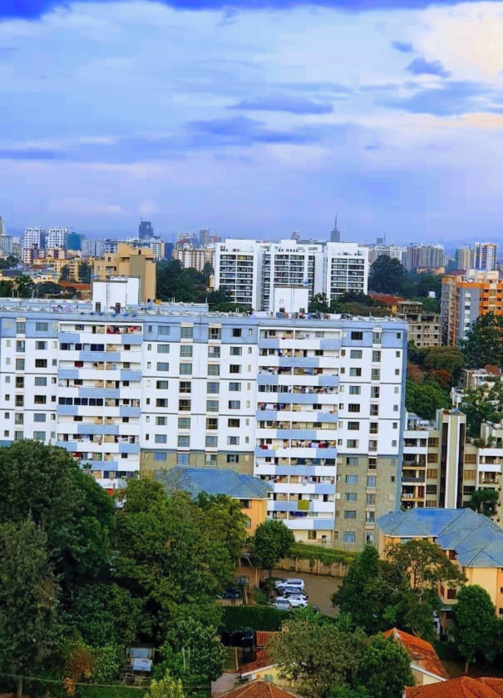 Un edificio residencial de varios pisos con balcones, rodeado de otros edificios y vegetación.