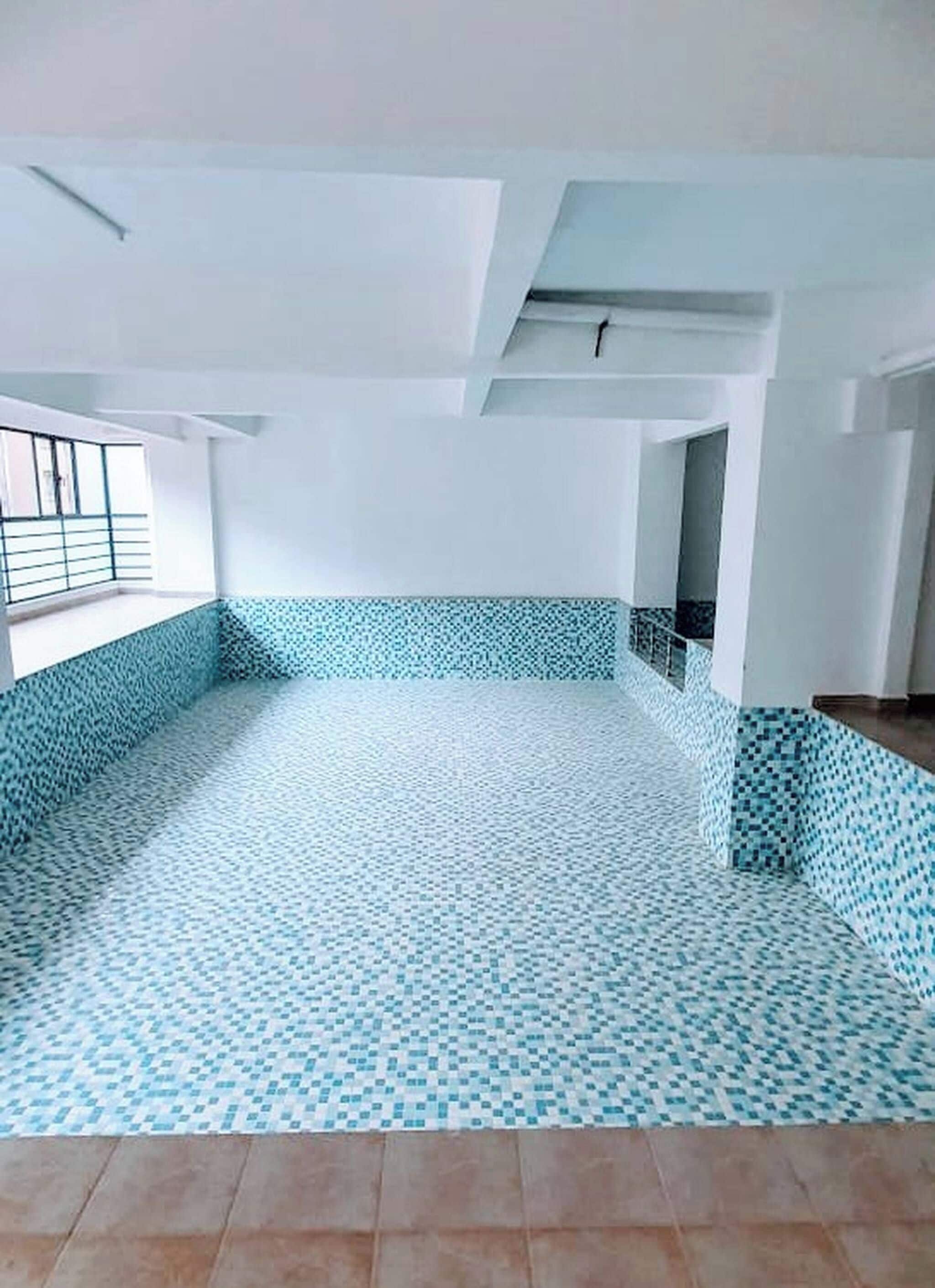 Um quarto vazio com chão de azulejos, paredes brancas e uma janela com grade de metal.