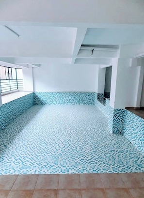 Een lege kamer met een betegelde vloer, witte muren en een raam met een metalen hekwerk.
