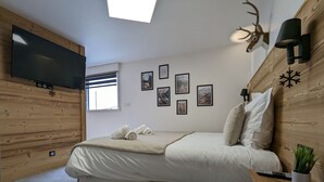 A bedroom with a bed, a mounted TV, a window, and wall-mounted lights.