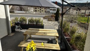 A patio with a wooden table and chairs, a barbecue grill, and a large umbrella.