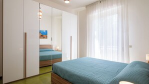 Un dormitorio con cama, armario, espejo y ventana con cortinas.