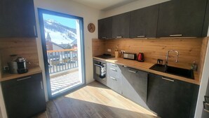 Une cuisine moderne avec des meubles de couleur sombre, un plan de travail en bois et une vue sur un paysage enneigé par le biais d’une porte vitrée.