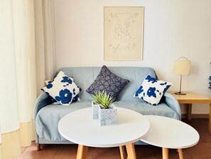 A living room with a grey sofa, two white round tables, a potted plant, and a lamp on a side table.