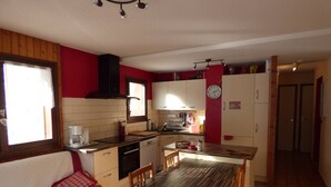 Eine kleine Küche mit Essbereich, Holzschränken, einer roten Wand und einer Uhr.