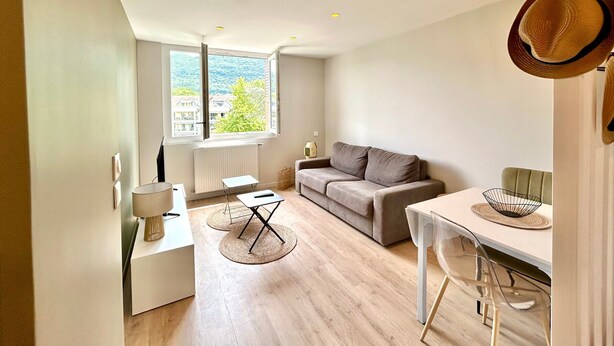 A modern living room with a sofa, a dining table, and a kitchen area.