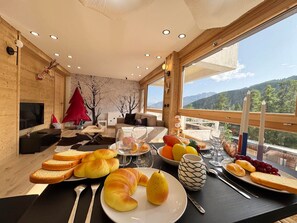 A dining area with a table set for breakfast, including croissants, bread, fruit, and a vase.