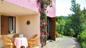 A patio with wicker chairs and a table, a pink wall, and a garden with red flowers. - Villa Bithia SaBratza Vacanze (Domus de Maria)