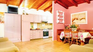A kitchen with pink cabinets, a dining area with a table and chairs, and a TV mounted above the cabinets. - Villa Bithia SaBratza Vacanze (Domus de Maria)