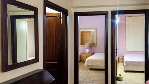 A hotel room with a wooden dresser, a bed with a white bedspread, a nightstand with a lamp, and a large mirror on the wall. - Villa Bithia SaBratza Vacanze (Domus de Maria)