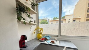 A small kitchen area with a window, a red kettle, a yellow vase with flowers, a plate of watermelon, a cup, and a chair. - Juan-les-Pins, Antibes - 3-bedroom apartment near beaches and town center (Antibes)