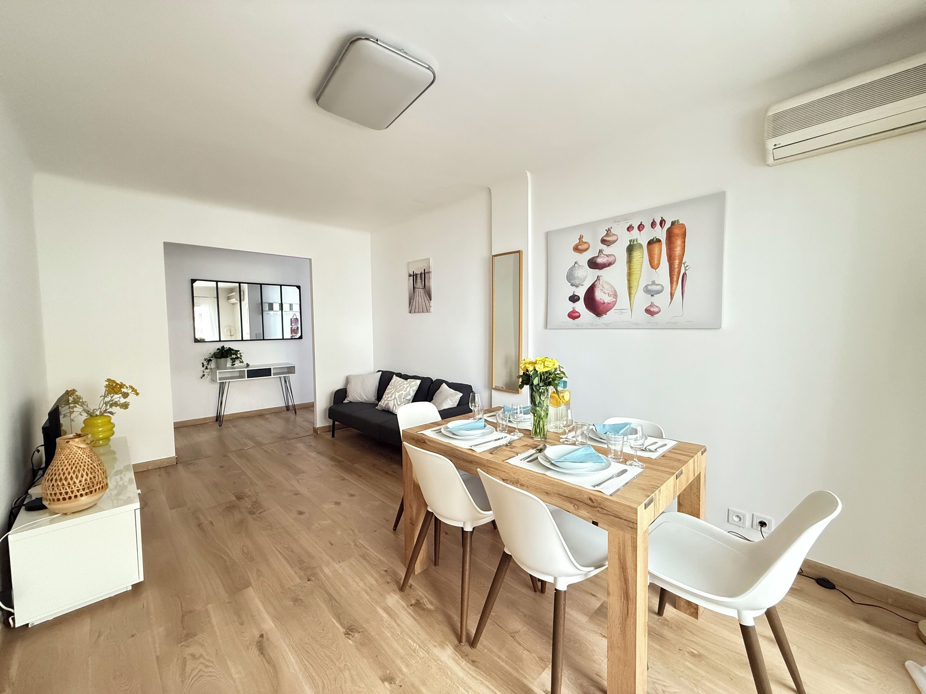 Ein modernes Wohnzimmer mit Essbereich, mit einem Holztisch, weißen Stühlen, einem schwarzen Sofa und einem großen Spiegel.