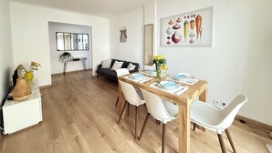 A modern living room with a dining area, featuring a wooden dining table, white chairs, a black sofa, and a large mirror. - Juan-les-Pins, Antibes - 3-bedroom apartment near beaches and town center (Antibes)